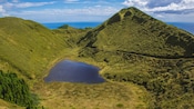 A lake located in a valley between grassy mountains overlooking the sea