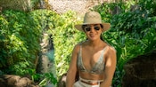 A woman wearing a hat and sunglasses in a lush tropical setting