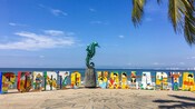 A boardwalk with a bronze statue of a person riding a sea horse next to artistic blocks that read Puerto Vallarta