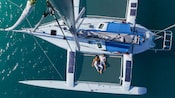 A couple and a child relaxing on the netting platform of a catamaran