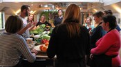 A group of people watch a cooking demonstration in a professional kitchen