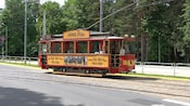 A trolley car riding on a track near a forest of trees