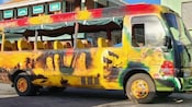 A colorful bus featuring the characters from the Pirates of the Caribbean movie parked in front of a building