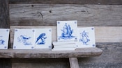 A display of tiles with images of birds, ships and more painted on them