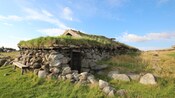 A reconstructed ancient stone building with a grass roof