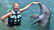 A woman in a life vest posing next to a dolphin while touching its nose at Basseterre in Saint Kitts