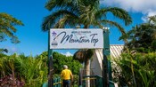 A tropical setting with a sign that reads ‘World Famous Mountain Top’