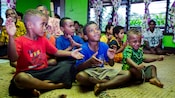 A group of children clapping while sitting on the floor of a Fijian schoolhouse