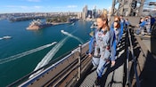 Um grupo sorridente de pessoas passeando na Ponte da Baía de Sydney com vista para a Baía de Sydney e para a Opera House