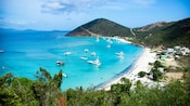 Boats anchored off the shore of a secluded beach surrounded by sloping hills