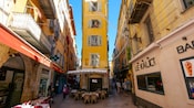 A small plaza between buildings, featuring 2 outdoor cafes and several shops