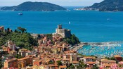 View of an ancient village with a castle, sailboats in a harbor and islands in the distance