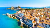 The coastal town of Corfu, Greece, with terracotta roofed buildings, sailboats docked in a harbor and a fortress on a peninsula