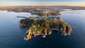 A craggy islet next to a mainland with rolling hills and mountains