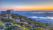 A contemporary stone and glass building on a rocky summit overlooking a river