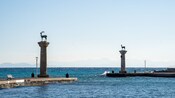Two stone columns with deer statues stand at the entrance of a harbor leading to the sea