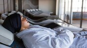 A woman in a bathrobe relaxing on a lounge chair in a spa setting with natural light