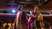 Two performers in African inspired costumes singing and dancing among Guests eating dinner during Pride Lands: Feast of The Lion King