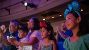 Dos niñas sonrientes con diademas viendo un espectáculo con sus padres y su hermano pequeño