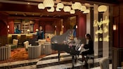 A piano bar on the Disney Treasure with 2 Cast Members serving drinks, a pianist and cabaret style seating