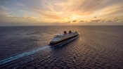 A Disney Cruise Line ship sails along in tranquil, open water, with a beautiful sunset in the background