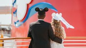 Una pareja con sombreros de orejas de Minnie Mouse y Mickey Mouse con temática de novios en la cubierta superior de un crucero de Disney