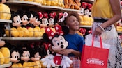 A young girl holds a Minnie Mouse plush in front of a wall of other plushes at Disney Springs