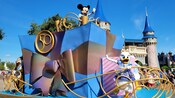 Riding a float that boasts an large, ornately wrapped gift and a large medallion with the number 50 in it, Mickey Mouse and Daisy Duck wave to Guests