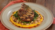 A grilled pork chop served over a bed of beans, greens and sweet potato puree