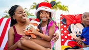 A mother and daughter smiling while holding a plush doll and wearing a Christmas themed Mickey Mouse hat