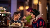 Disney Princess Snow White sits with a young Guest at Artist Point as they share a laugh