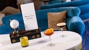 Una mesa con 3 cócteles y un menú en cuyo frente se lee “Belle Vue Lounge” en Disney’s BoardWalk Inn.
