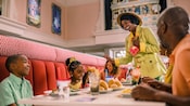 A father and 2 children laughing with Princess Tiana at a dining table at the Nineteen Hundred Park Fare restaurant