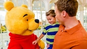 A man holding his child in his arms while talking to Winnie the Pooh in The Crystal Palace