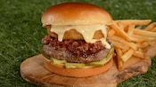 A burger with bacon, pickles, an onion ring and cheese between 2 buns with a side of fries
