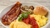 Une assiette de déjeuner avec œufs brouillés, bacon croustillant, saucisse et petit pain