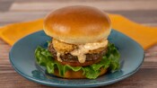 A hamburger with lettuce, tomato, fried shrimp and sauce on a plate