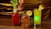 Trois cocktails servis avec des fruits sur un bar