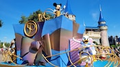 Riding a float that boasts an large, ornately wrapped gift and a large medallion with the number 50 in it, Mickey Mouse and Daisy Duck wave to Guests