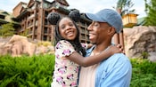 A little girl wears a Minnie Mouse headband and smiles with her dad outside of Disney’s Wilderness Lodge
