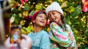 2 young Guests pose for a picture in front of a Christmas tree at Walt Disney World Resort 
