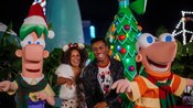 A man and woman standing in between Phineas and Ferb in front of a Christmas tree 