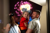 A father holds his daughter in his arms while they smile as fireworks burst behind them