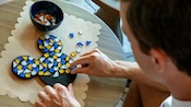 A man gluing stones onto a Mickey Mouse shaped object to create a mosaic art piece 