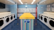 A laundry room with 2 rows of washing machines and a bank of dryers against the back wall