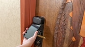 A hand holding a smartphone to a room door lock at Disney's Animal Kingdom Lodge