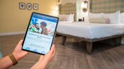 Unas manos sostienen una tableta que muestra el sitio web de Walt Disney World Resort en una habitación de Disney’s BoardWalk Inn