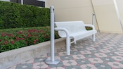 A modern park bench sits in front of a flower bed and manicured shrubbery