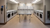 A laundry room with 2 rows of washing machines and a bank of dryers against the back wall