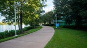 A sidewalk bordered by a manicured lawn between Disney’s Pop Century Resort and a serene lake